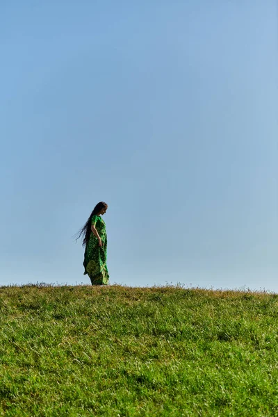 Summer, ethnic heritage, young indian woman under blue cloudless sky in green field — Stock Photo