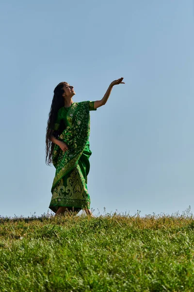Summer, sunny day, joyful indian woman in sari standing with outstretched hand under blue sky — Stock Photo
