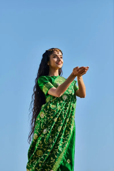 Summer, sunny day, joyful asian woman with outstretched hands standing in sari under blue sky — Stock Photo