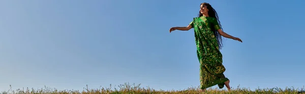 Безтурботне літо, елегантна індійська жінка в традиційному сарі біжить під блакитним безхмарним небом, банер — стокове фото