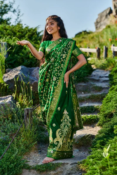 Jovem mulher indiana alegre em sari posando em escadas de pedra no parque verde no fundo — Fotografia de Stock
