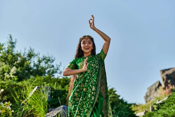Excitada mujer india joven en elegante sari verde posando en el parque de verano en el fondo - foto de stock