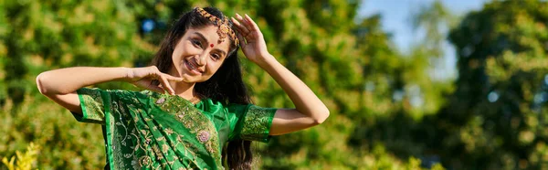 Cheerful and stylish indian woman in traditional outfit posing and standing in park, banner — Stock Photo