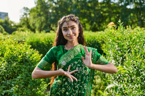 Стильная молодая индианка в сари и бинди позирует и смотрит в камеру в парке — стоковое фото