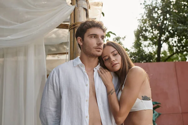 Mujer tatuada apoyada en el hombro del novio en camisa blanca durante las vacaciones de verano, romance - foto de stock
