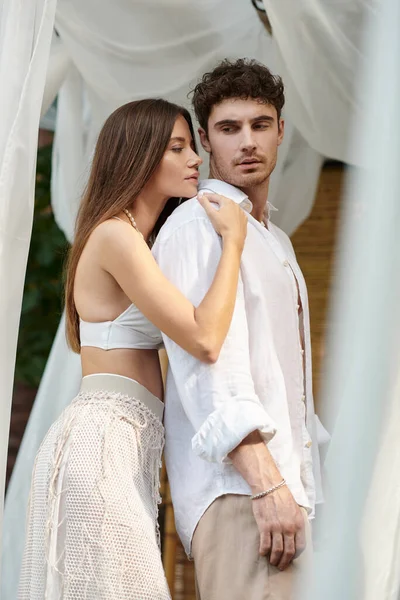 Momento íntimo, mujer abrazando hombre guapo cerca de tul blanco del pabellón privado, vacaciones de verano - foto de stock