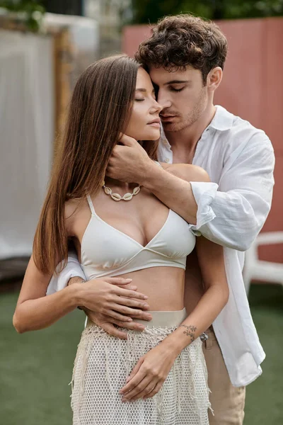 Guapo hombre abrazando tatuado novia en crop top y de pie juntos al aire libre, romance - foto de stock