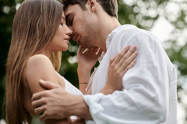 Vista lateral del hombre besando novia en la parte superior de la cosecha y de pie juntos al aire libre, pareja romántica - foto de stock