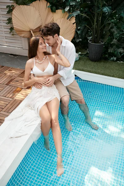 Coppia allegra in abiti bianchi seduti insieme a bordo piscina durante le vacanze, fuga romantica — Foto stock