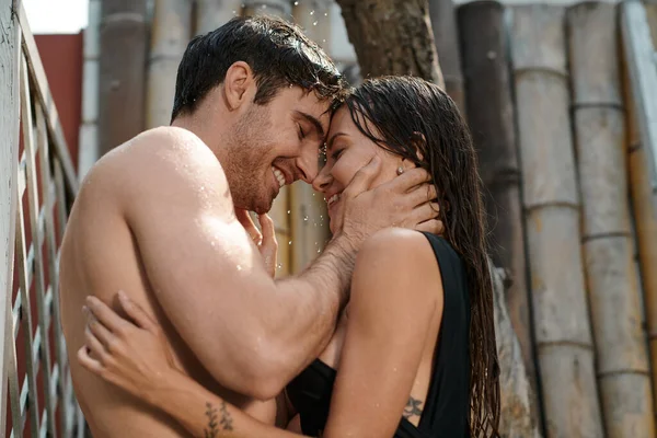Сексуальная пара, обнимающаяся под струями воды, веселые влюбленные, принимающие душ и улыбающиеся на открытом воздухе — стоковое фото