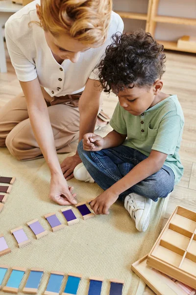 Montessori color box, material touch box, blonde frau und afrikanisch-amerikanischer junge, lehrer, kind — Stock Photo