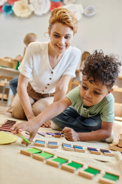Montessori material, menino americano africano inteligente jogando jogo de cor educacional perto professor orgulhoso — Fotografia de Stock