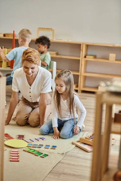 Maestra y linda niña preescolar jugando juego montessori, mujer y niños, chicos interracial - foto de stock