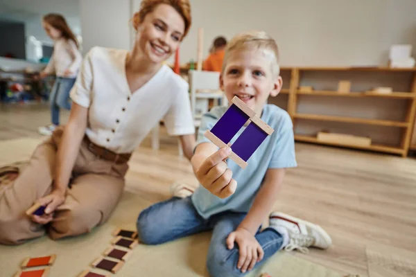Школа montessori, веселый мальчик играет в цветовую игру рядом с учительницей, сидя на полу — стоковое фото