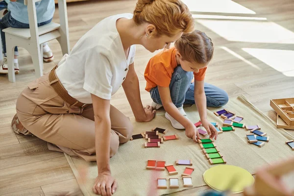 Концепция montessori, девочка играет в цветовую игру рядом с веселой учительницей, сидящей на полу — стоковое фото