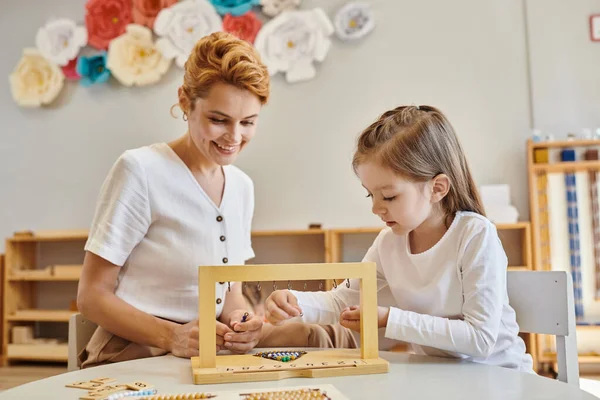 Kleiderbügel für Farbperlentreppen, Montessori-Konzept, nettes Mädchen spielt pädagogisches Spiel in der Nähe des Lehrers — Stockfoto