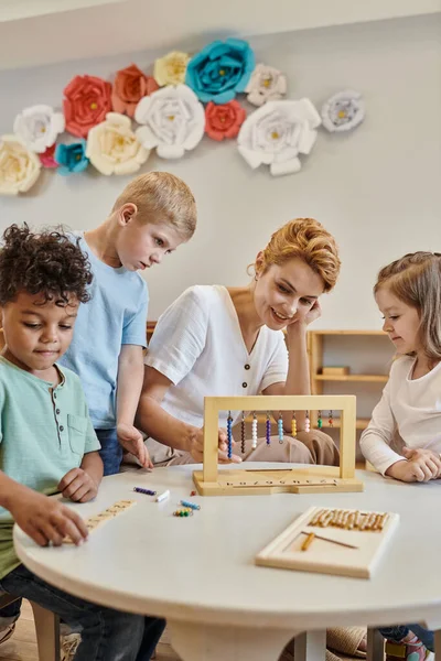 Концепция montessori, учительница рядом с межрасовыми детьми, играющая в развивающие игры, разнообразные мальчики — стоковое фото