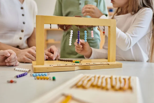 Percha para escaleras de cuentas de color, concepto montessori, vista recortada de los niños jugando juego cerca del maestro - foto de stock