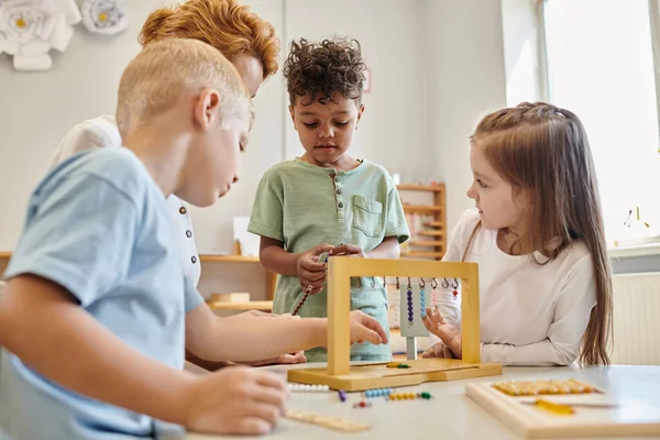 Cute kids looking at african american boy playing educational game in montessori school, diversity — Stock Photo
