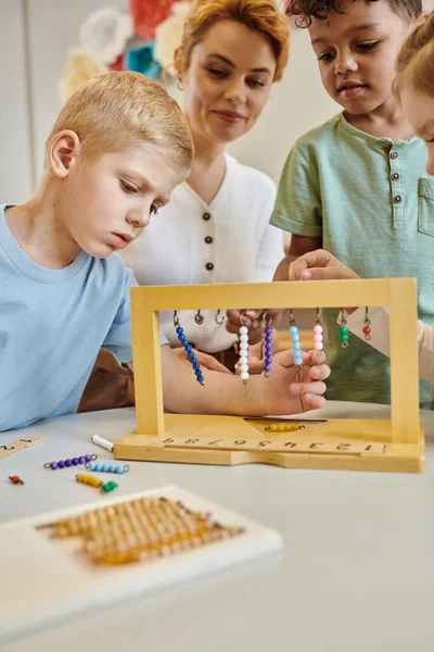 Montessori school, multicultural kids playing with color bead stairs near teacher, diversity — Stock Photo