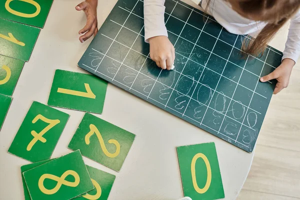 Top view of girl writing number zero on chalkboard, learning how to count in Montessori school — Stock Photo