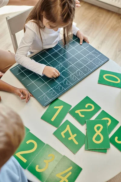 Top view of girl writing numbers on chalkboard, learning how to count in Montessori school — Stock Photo