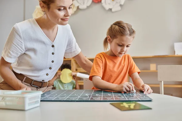 Glückliche Lehrerin beobachtet intelligentes Mädchen in Montessori-Schule, zählt, schreibt auf Tafel, Zahlen — Stockfoto
