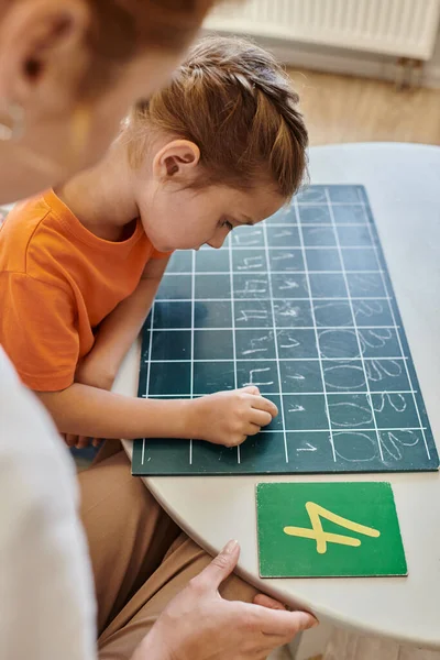 Female teacher observing smart girl in Montessori school, counting, writing on chalkboard, numbers — Stock Photo