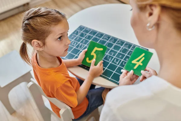 Clever girl and teacher holding numbers near chalkboard, learning through play, counting, top view — Stock Photo