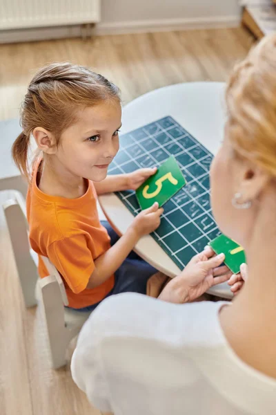 Clever girl and teacher holding numbers near chalkboard, learning through play, math, top view — Stock Photo