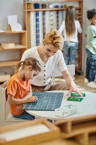 Mädchen schreiben auf Kreidetafel neben Zahlen, Lernen durch Spiel, Lehrer und Kinder Montessori-Konzept — Stockfoto