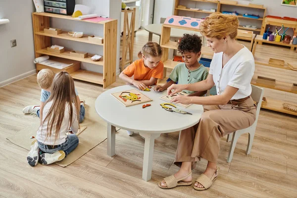 Female teacher using didactic montessori material while playing with interracial kids, diversity — Stock Photo