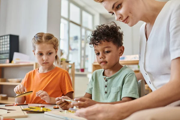 Interracial children playing with didactic montessori material near female teacher, diversity — Stock Photo