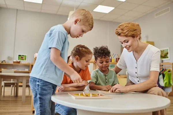 Smiling teacher and interracial kids playing with didactic material in class in montessori school — Stock Photo