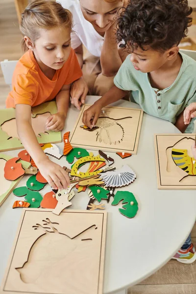 Hochwinkelaufnahme multiethnischer Kinder, die in der Nähe des Lehrers während des Unterrichts in der Montessori-Schule spielen — Stockfoto