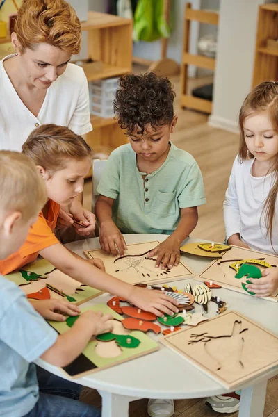 Niños multiétnicos y profesor jugando con materiales didácticos en la escuela montessori - foto de stock