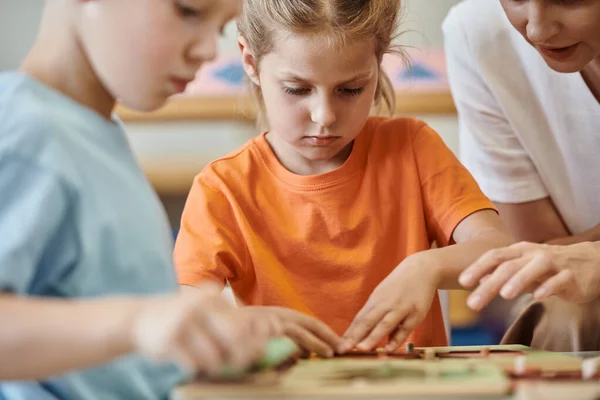 Lehrer im Gespräch mit Kindern in der Nähe verschwommener Unterrichtsmaterialien in der Montessori-Schule — Stockfoto