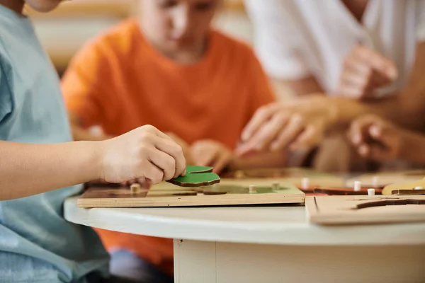 Vista recortada de niños jugando con materiales didácticos cerca de profesor borroso en la escuela montessori - foto de stock