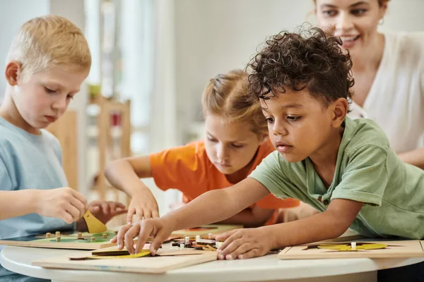 Criança afro-americana brincando com material didático perto de crianças e professor na escola montessori — Fotografia de Stock