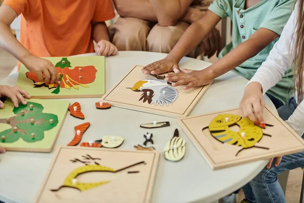Abgeschnittene Ansicht von interrassischen Kindern, die mit didaktischen Materialien in der Nähe des Lehrers in der Montessori-Schule spielen — Stockfoto
