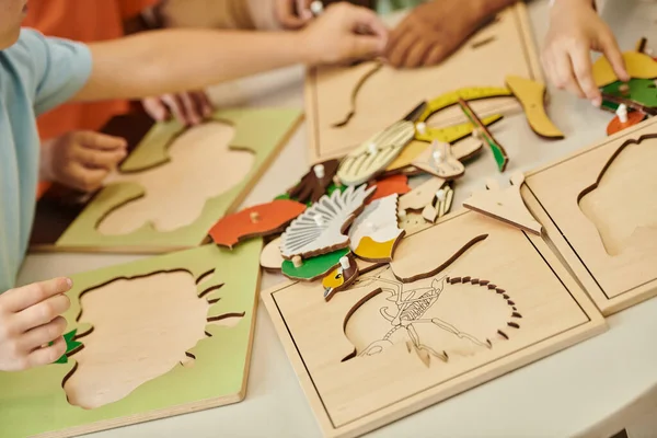 Vista recortada de niños interracial jugando con materiales didácticos en la mesa en la escuela montessori - foto de stock