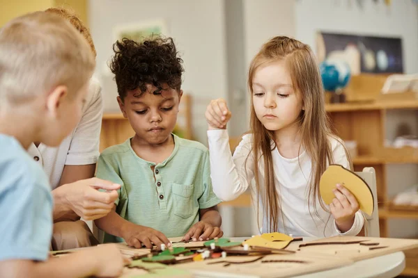 Girl playing with didactic material near interracial kids and teacher in montessori school — Stock Photo