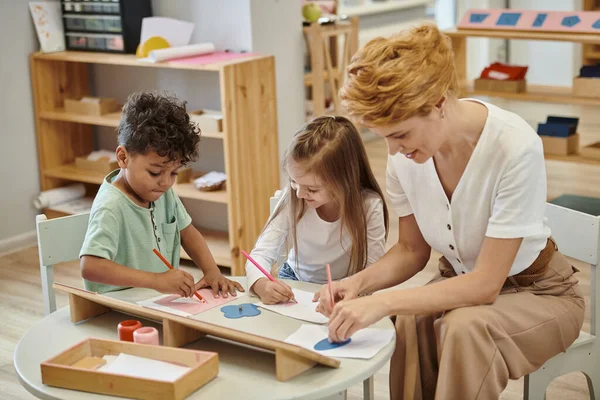 Lächelnder Lehrer und multiethnische Kinder zeichnen während des Unterrichts in der Montessori-Schule — Stockfoto