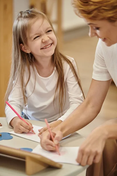 Menina alegre pintura e olhando para professor desfocado durante a lição na escola montessori — Fotografia de Stock