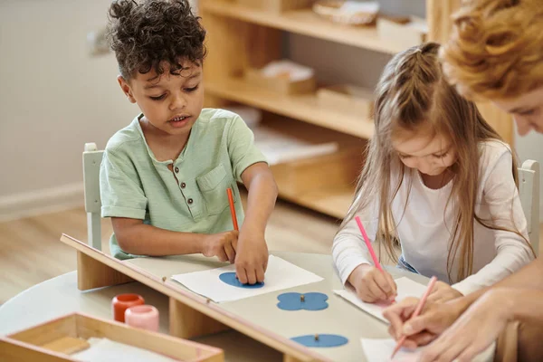 Africano americano ragazzo pittura vicino amico e offuscata insegnante in montessori scuola — Foto stock