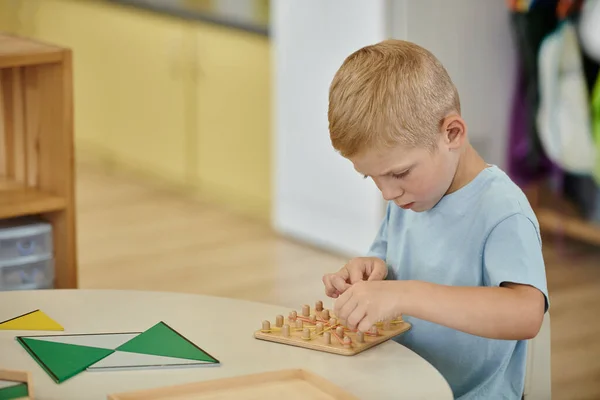 Boy playing with rubber bands and wooden board on table during lesson in montessori school — Stock Photo