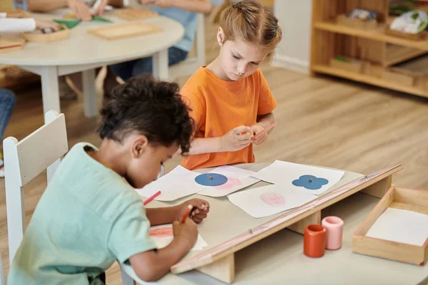 Niños multiétnicos dibujo con lápices en la mesa en la clase de la escuela montessori - foto de stock