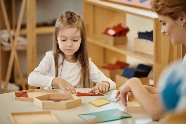 Lächelnder Lehrer beim Spielen mit Mädchen und Lehrmaterial auf dem Tisch in der Montessori-Schule — Stockfoto