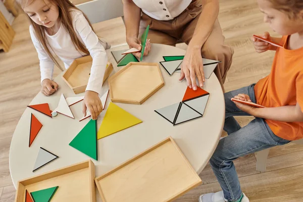 Visão de alto ângulo de professor e crianças brincando com triângulos na mesa na escola montessori — Fotografia de Stock