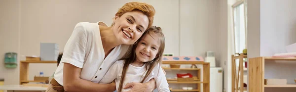 Positive teacher and pupil looking at camera together in class in montessori school, banner — Stock Photo